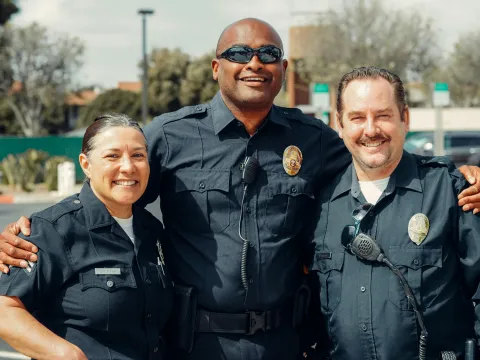 Photo of three law enforcement officers arm in arm smiling at the camera